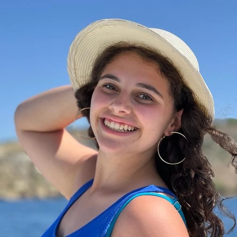 Monica smiling in a wide-brimmed sun hat under a blue sky